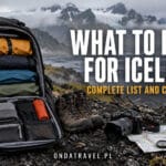 Open travel backpack with waterproof clothing, boots and map on Icelandic volcanic ground.