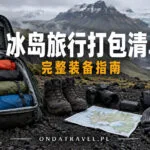 Mochila abierta con ropa impermeable, botas y mapa sobre suelo volcánico de Islandia.